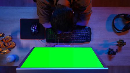 Photo for Gaming and streaming concept. Top view of man sitting at the desk hands on keyboard napping tired, computer monitor with Chroma key green screen, advertising area workspace mockup. - Royalty Free Image