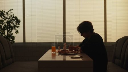 Photo for Everyday life and people relationships concept. Portrait of person in cafeteria. Silhouette of adult male sitting at the bistro bar, man having dinner alone, eating pizza and drinking juice. - Royalty Free Image
