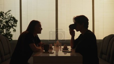 Photo for Everyday life and people relationships concept. Portrait of couple in cafeteria. Silhouette of male and female sitting at the food bistro bar together, man drinking coffee girl talking to him. - Royalty Free Image