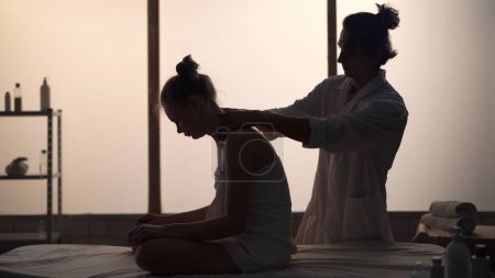 Masseur, massage specialist giving back massage to his patient. Silhouettes of a woman and a man in the massaging room, spa procedure. Healthcare, medical treatment, holistic therapy.