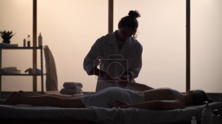 Photo for Masseur, massage specialist giving back and arm massage to his patient. Silhouettes of a woman and a man in the massaging room, spa procedure. Healthcare, medical treatment, holistic therapy. - Royalty Free Image