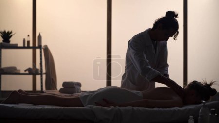 Téléchargez les photos : Masseur, spécialiste du massage qui donne un massage du cou à son patient. Silhouettes d'une femme et d'un homme dans la salle de massage, procédure spa. Soins de santé, traitement médical, thérapie holistique. - en image libre de droit