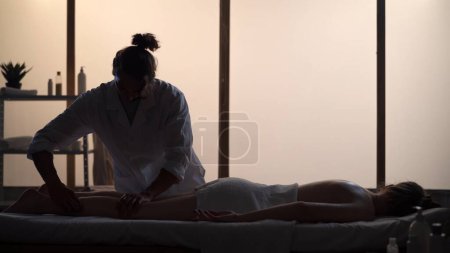 Téléchargez les photos : Masseur, spécialiste du massage offrant un massage complet du corps à son patient. Silhouettes d'une femme et d'un homme dans la salle de massage, procédure spa. Soins de santé, traitement médical, thérapie holistique. - en image libre de droit