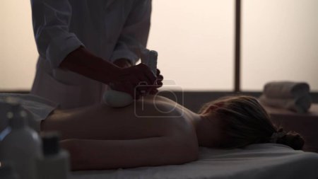 Photo for Masseur, massage specialist giving a massage to his patient using herbal bags. Silhouettes of a woman and a man in the massaging room, spa procedure. Healthcare, medical treatment, holistic therapy. - Royalty Free Image