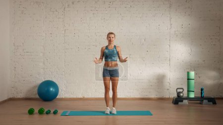 Photo for Personal sport classes at home online. Blonde female in sportswear doing exercises. Healthcare creative advertisement concept. Woman fitness coach in the room looking at the camera and talking. - Royalty Free Image