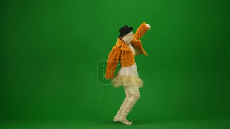 Glamorosa momia baila en un abrigo de piel naranja, sombrero y gafas de sol. Tecla de croma aislada de pantalla verde. Mock up, espacio de trabajo, publicidad. Longitud total. Media vuelta. Halloween vacaciones.