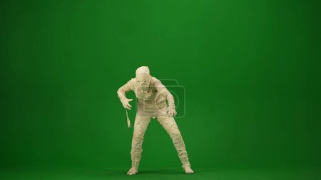 Foto de Foto de croma key aislada en pantalla verde que captura una momia tambaleándose, caminando hacia la cámara con los brazos extendidos. Prepárate, espacio de trabajo para tu clip de promoción o anuncio. Longitud completa. - Imagen libre de derechos