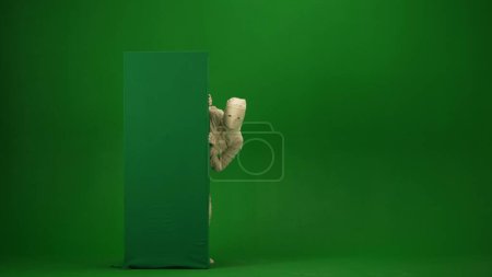 Photo for Green screen isolated chroma key photo capturing a mummy peeking from behind a green screen banner box. Mock up, workspace for your promotion clip or advertisement. Full length. - Royalty Free Image
