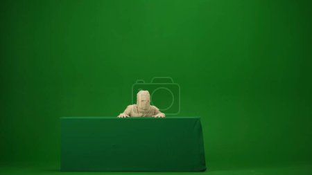 Foto de Fotografía de croma clave aislada de pantalla verde que captura una momia que se levanta y mira desde detrás de una caja de banner de pantalla verde. Prepárate, espacio de trabajo para tu clip de promoción o anuncio. Longitud completa. - Imagen libre de derechos
