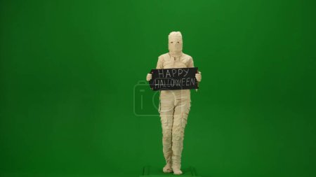 Photo for Green screen isolated chroma key photo capturing a mummy holding a chalkboard with happy halloween on it. Mock up for your promotion clip or advertisement. Full length. - Royalty Free Image