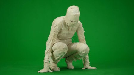 Photo for Green screen isolated chroma key photo capturing a mummy squatting, holding onto the ground, as if its going to stand up. Mock up, workspace for your promotion clip or advertisement. Full length. - Royalty Free Image
