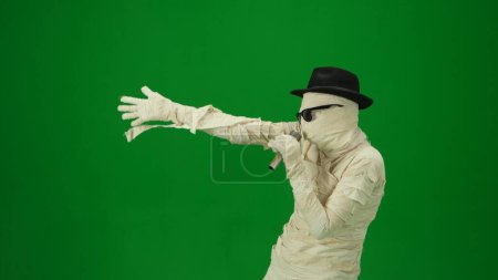 Pantalla verde aislada croma clave foto captura de una momia con gafas de sol y un sombrero cantando en el micrófono. Prepárate para tu clip de promoción o anuncio. Vacaciones de Halloween. Tamaño medio.