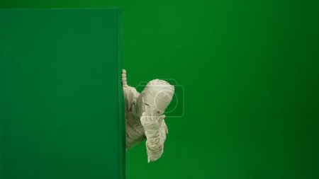 Photo for Green screen isolated chroma key photo capturing a mummy peeking from behind a green screen banner box calling somebody with its hand. Medium size. Mock up for your promotion clip or advertisement. - Royalty Free Image