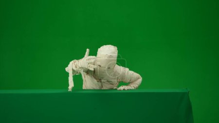 Photo for Green screen isolated chroma key photo capturing a mummy rising from behind a green screen banner box, calling somebody with its hand. Medium size. Mock up for your promotion clip or advertisement. - Royalty Free Image