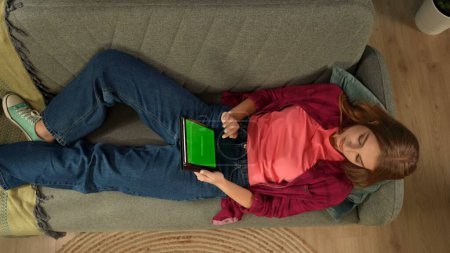 Foto de Vista superior de la captura de una mujer joven acostada en el sofá, mirando a la pantalla de la tableta con un área de publicidad, espacio de trabajo se burlan de ella. Ocio, compras online, redes sociales y comunicación. - Imagen libre de derechos