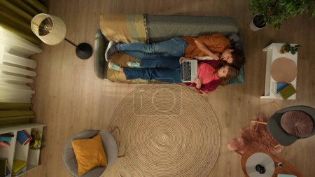 Foto de Vista superior de la captura de una joven pareja acostada en el sofá, abrazos y hablar, mirando a la pantalla del ordenador portátil como si estuvieran buscando algo en línea. Familia, ocio, compras en línea, social - Imagen libre de derechos