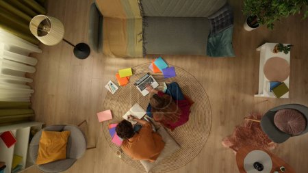 Photo for Top view capturing a young couple sitting on the floor next to each other and studying, working on a laptop and taking notes, surrounded with colorful books. Dating, education, spending time together. - Royalty Free Image
