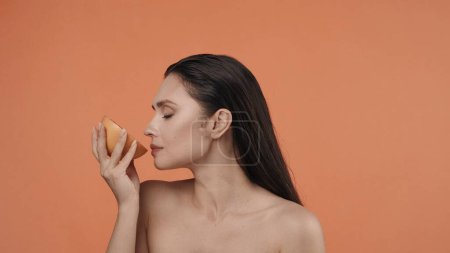 Photo for Portrait of attractive brunette model. Close up shot of a female with pure makeup. Skincare creative concept. Appealing woman holding half sliced fresh grapefruit and smells it, eyes closed. - Royalty Free Image