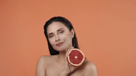 Photo for Portrait of attractive brunette model. Close up shot of a female with pure makeup. Skincare creative concept. Appealing woman holding sliced grapefruit and posing smiling at the camera. - Royalty Free Image