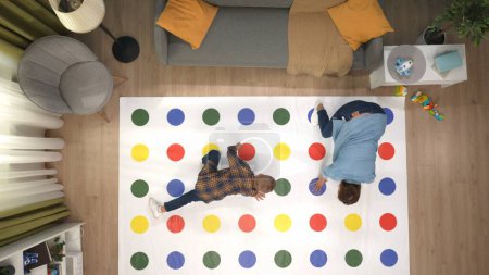 Photo for Senior family members life concept. Portrait of family together. Top view of apartment room, twister game laying on the floor, adult mom and son playing together, stepping on colorful areas. - Royalty Free Image