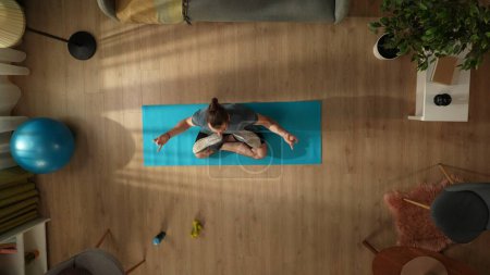 Téléchargez les photos : Vue de dessus capturant un jeune homme faisant son exercice de yoga matinal, méditant dans une pose de lotus. Maison, chambre, activités intérieures. Mode de vie sain et actif, routine matinale, atteindre les objectifs. - en image libre de droit
