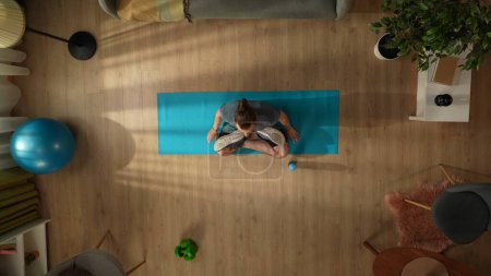 Foto de Vista superior de la captura de un joven haciendo su ejercicio de yoga por la mañana, sentado en una pose de loto. Hogar, sala, actividades cubiertas. Estilo de vida saludable y activo, rutina matutina, alcanzar los objetivos. - Imagen libre de derechos