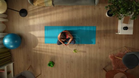 Foto de Vista superior de la captura de una mujer joven haciendo su ejercicio de yoga por la mañana, sentado en una pose de loto. Hogar, sala, actividades cubiertas. Estilo de vida saludable y activo, rutina matutina, alcanzar los objetivos. - Imagen libre de derechos