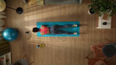 Photo for Top view capturing a young woman doing her morning exercise, standing in a plank with a timer on her smartphone. Indoor activities. Healthy and active lifestyle, morning routine, achieving the goals. - Royalty Free Image