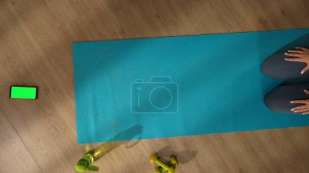 Photo for Top view capturing an unrecognizable woman sitting on a mat in front of a smartphone with an advertising area, workspace mock up on it. Healthy and active lifestyle, achieving the goals. - Royalty Free Image