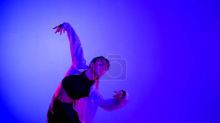 Foto de Mujer joven vistiendo un top, pantalones cortos y una camisa realizando danza contemporánea emocional en el estudio. Esquema de color azul neón, rosa y rojo, ombre, fondo degradado. De tamaño medio. - Imagen libre de derechos