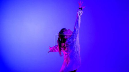 Photo for Young woman wearing a top, shorts and a shirt performing emotional contemporary dance in studio. Neon blue, pink and red color scheme, ombre, gradient background. Medium sized. - Royalty Free Image
