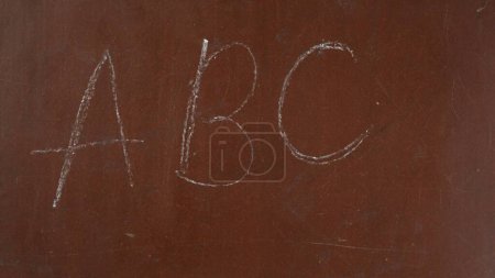 Foto de Fondo de pizarra marrón texturizado. A, B, C, las primeras letras del alfabeto están escritas en el tablero con un trozo de tiza blanca. De cerca. Contenido educativo y creativo, concepto escolar. - Imagen libre de derechos