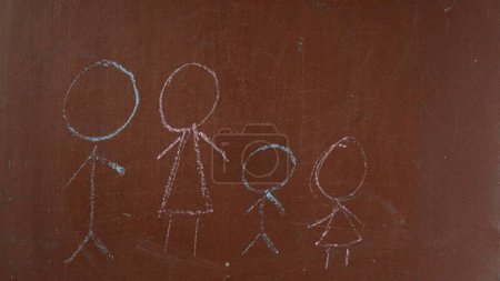 Foto de Fondo de pizarra marrón texturizado. Un dibujo infantil de una familia se dibuja en el tablero con un pedazo de tiza blanca. De cerca. Contenido educativo y creativo, concepto escolar. - Imagen libre de derechos