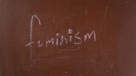 Téléchargez les photos : Fond de tableau brun texturé. Le féminisme est écrit sur le tableau avec un morceau de craie rose. Gros plan. Contenu éducatif et créatif, concept d'égalité. - en image libre de droit