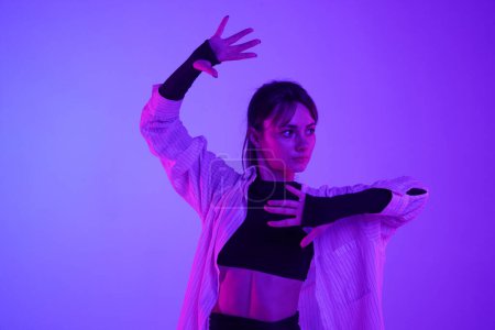 Photo for Young woman wearing a top, shorts and a shirt performing contemporary dance in studio. Neon pink and purple color scheme, ombre, gradient background. Medium sized. - Royalty Free Image