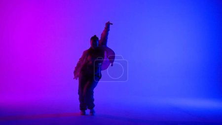 Foto de Atractiva mujer bailando jazz-funk sobre fondo de neón rosa y azul en un estudio. Coreografía de danza moderna dinámica y enérgica. Longitud total. Contenido creativo, clip promocional o publicidad. - Imagen libre de derechos