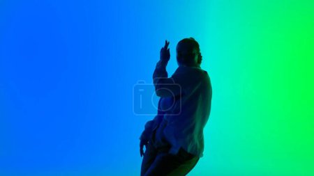 Photo for Silhouette of a woman dancing jazz-funk on green and blue neon background in a studio. Modern dynamic and energetic dance choreography. Medium full. Creative content, promotional clip or advertisement - Royalty Free Image
