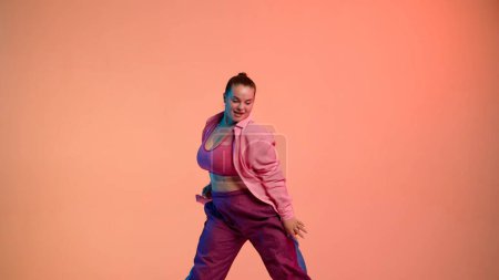 Photo for Attractive woman dancing jazz-funk on pink isolated neon background in a studio. Modern dynamic and energetic dance choreography. Medium full. Creative content, promotional clip or advertisement. - Royalty Free Image