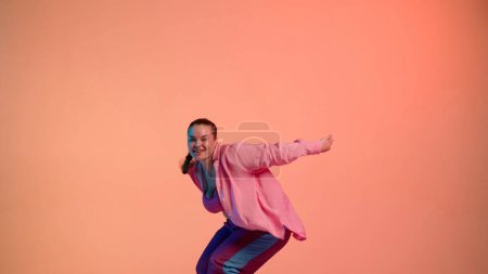 Foto de Mujer atractiva bailando jazz-funk sobre fondo de neón aislado rosa en un estudio. Coreografía de danza moderna dinámica y enérgica. Medio lleno. Contenido creativo, clip promocional o publicidad. - Imagen libre de derechos