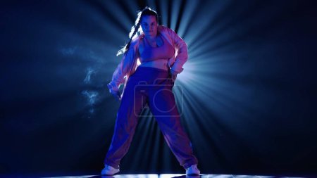 Photo for Silhouette of a woman dancing jazz-funk in a studio. Black background filled with smoke, white spotlight shining from behind. Modern choreography. Full length. Promotional clip or advertisement. - Royalty Free Image