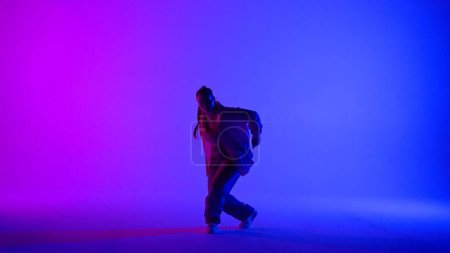 Foto de Atractiva mujer bailando jazz-funk sobre fondo de neón rosa y azul en un estudio. Coreografía de danza moderna dinámica y enérgica. Longitud total. Contenido creativo, clip promocional o publicidad. - Imagen libre de derechos