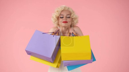 Foto de Joven mujer feliz sosteniendo bolsas de compras de colores. Mujer parecida a Marilyn Monroe en el estudio sobre fondo rosa. Concepto de compras, ventas, viernes negro - Imagen libre de derechos