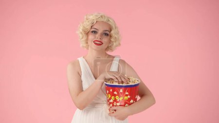 Foto de Mujer con un gran cubo de palomitas de maíz, disfrutando viendo una película. Mujer como Marilyn Monroe en estudio sobre fondo rosa - Imagen libre de derechos