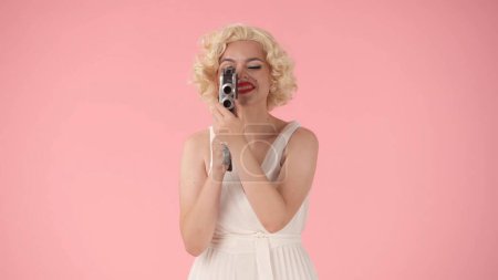 Foto de Mujer usando cámara de video retro de cerca. Mujer parecida a Marilyn Monroe en estudio sobre fondo rosa - Imagen libre de derechos