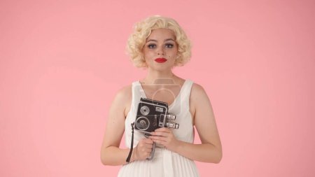 Photo for Portrait of woman with retro video camera in hands close up. Woman looking like Marilyn Monroe in studio on pink background - Royalty Free Image