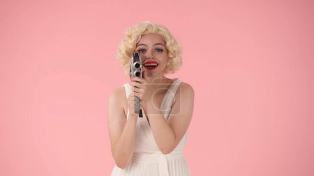 Photo for Woman uses retro video camera. Woman looking like Marilyn Monroe in studio on pink background - Royalty Free Image