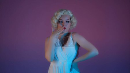 Foto de Retrato de una mujer encantadora a imagen de Marilyn Monroe de cerca. Mujer con maquillaje brillante en vestido blanco y peluca en estudio en luz de neón rosa y verde - Imagen libre de derechos