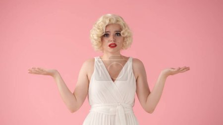 Photo for A woman spreads her hands in despair. A woman in the image of Marilyn Monroe in the studio on a pink background - Royalty Free Image