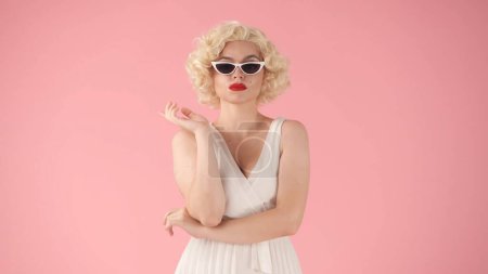 Foto de Retrato de una mujer en la imagen de Marilyn Monroe con gafas de sol en forma de ojo de gato en el estudio sobre fondo rosa - Imagen libre de derechos