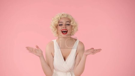 Photo for Young woman makes a victory gesture, celebrating her triumph. A woman in the look of Marilyn Monroe in the studio on a pink background - Royalty Free Image